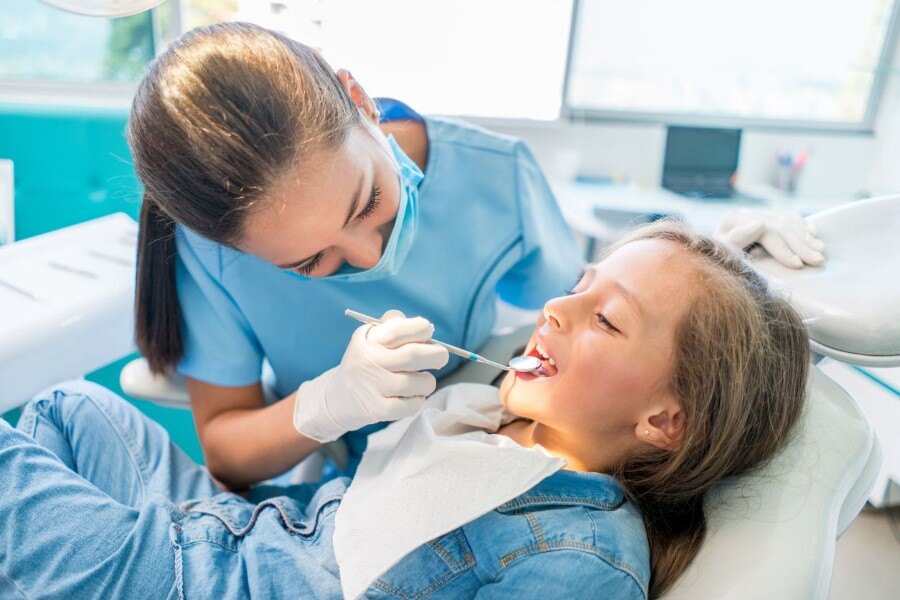 Young-girl-sitting-on-dental-chair-getting-her-teeth-checked-by-a-dentist