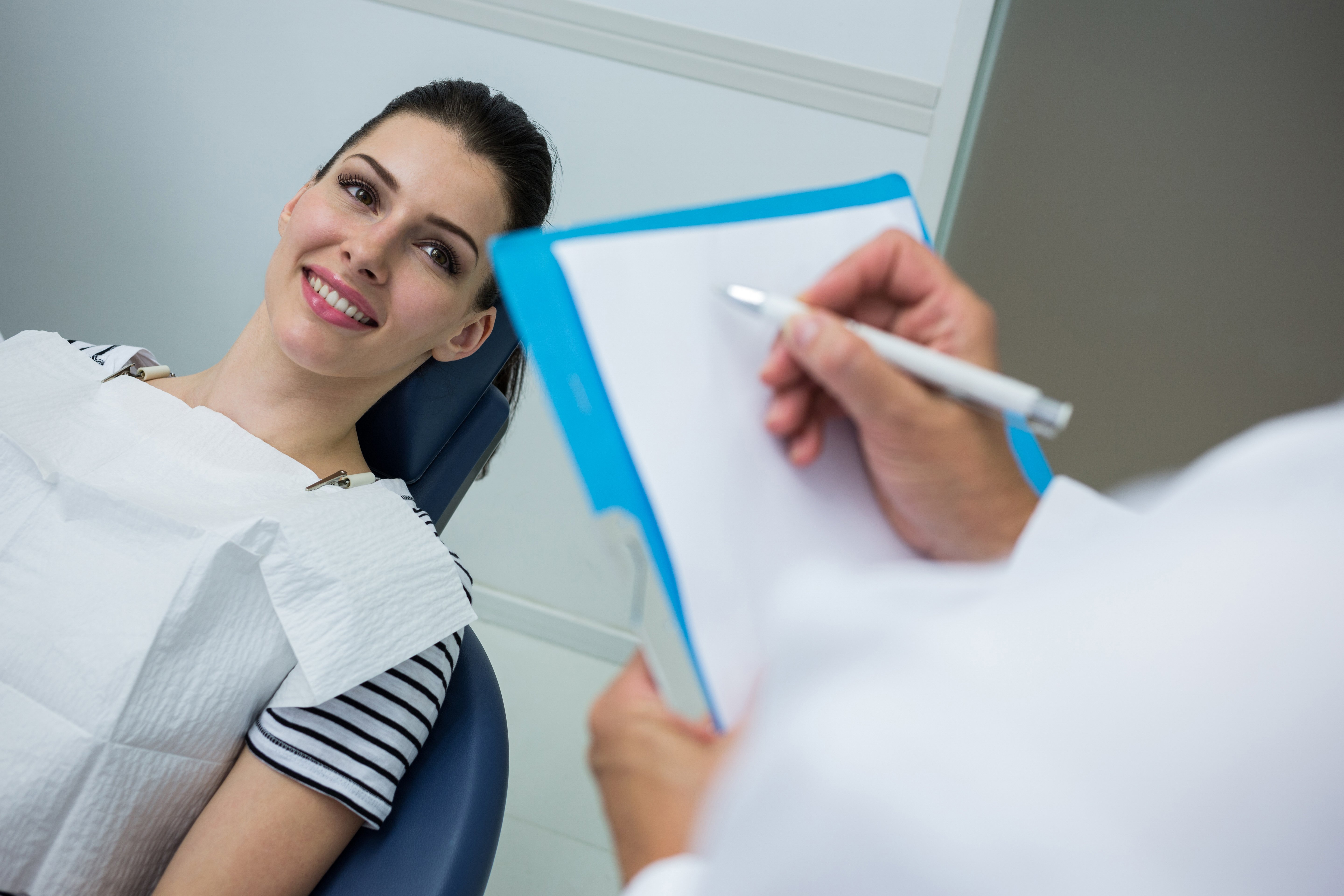 doctor-writing-clipboard-while-patient-lying-dental-bed