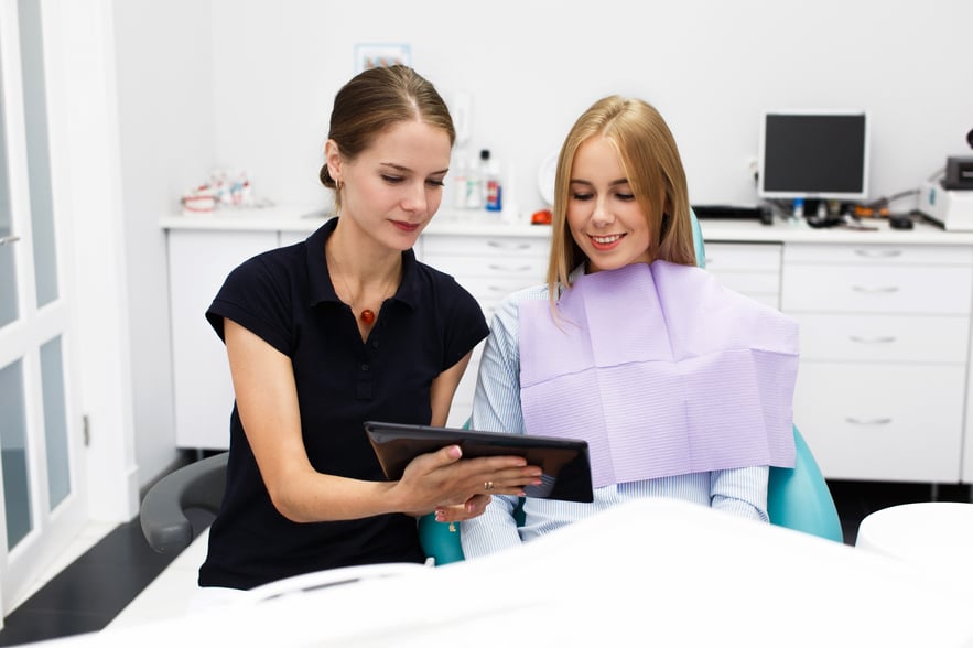 smiling-woman-sits-chair-dentist-office-while-doctor-shows-her-something