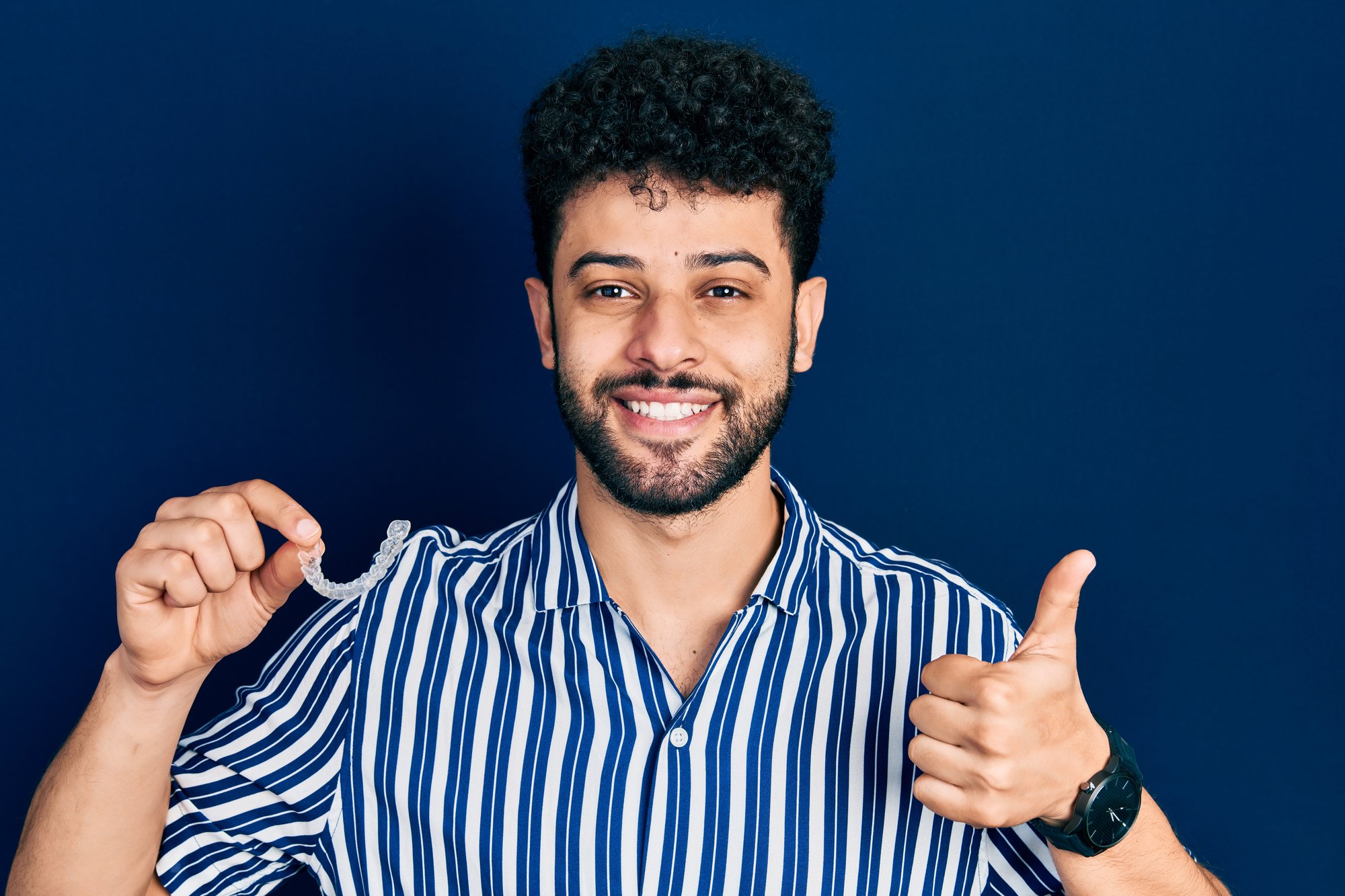 young-arab-man-with-beard-holding-invisible-aligner-orthodontic-braces-smiling-happy-positive-thumb-up-doing-excellent-approval-sign