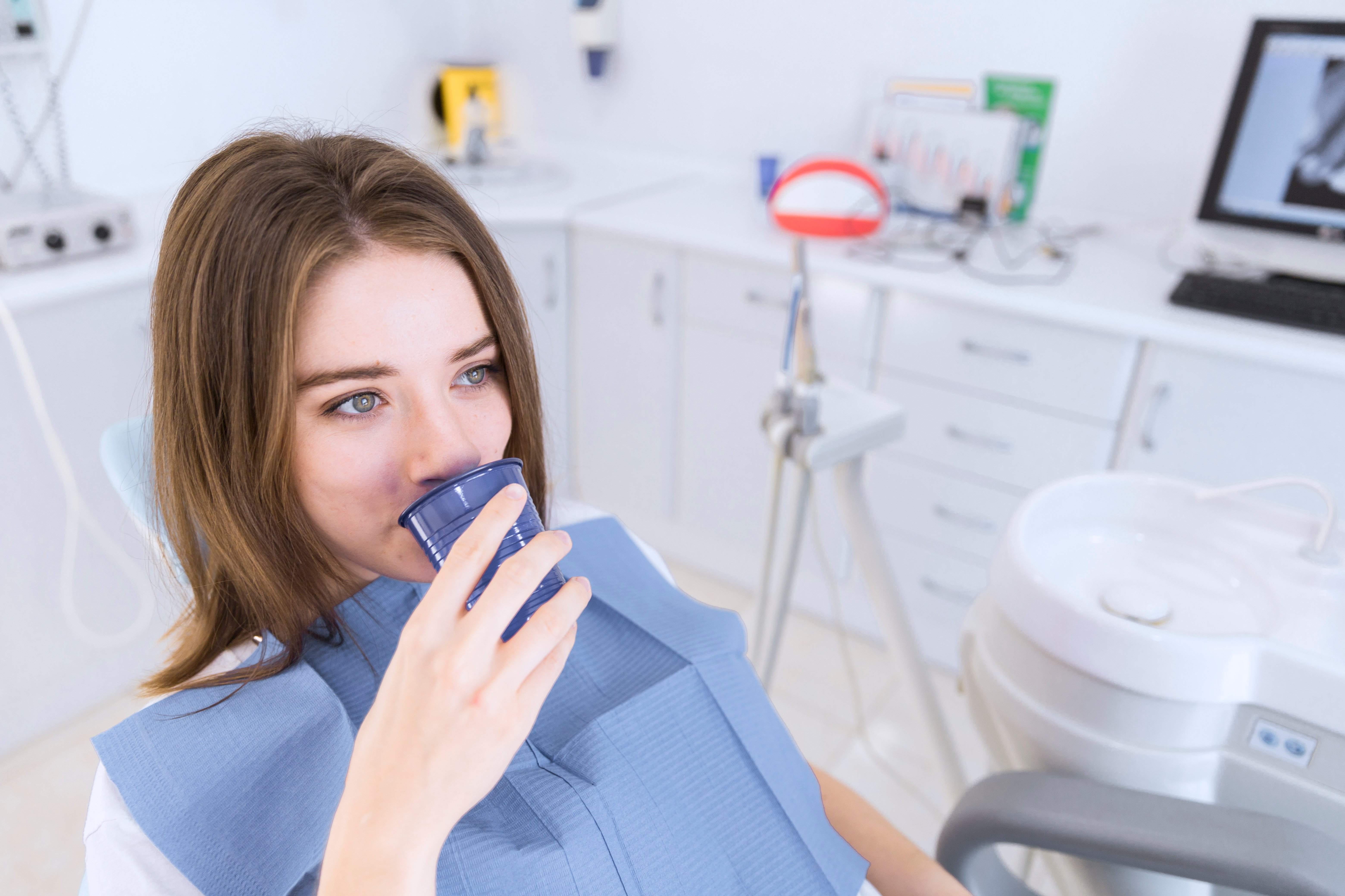 young-woman-taking-water-while-sitting-dental-chair